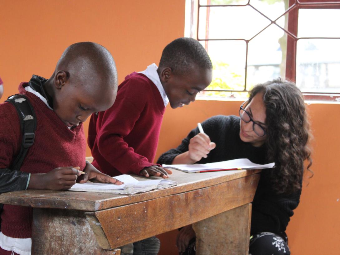 A young student gets assistance during class from a volunteer doing a teaching placement in Tanzania. A volunteer teaching abroad helps a child complete an activity at a school in Tanzania, Africa.